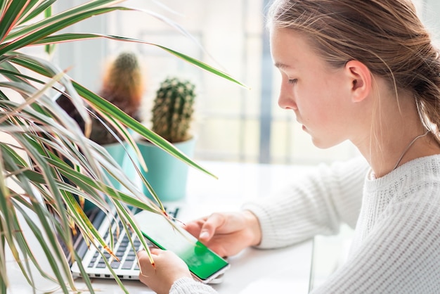 Beautiful young school girl working at home checking her phone with chromakey green screen