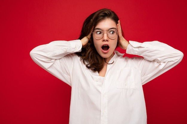 Photo beautiful young shocked amazed curly brunette woman wearing white shirt and optical glasses isolated