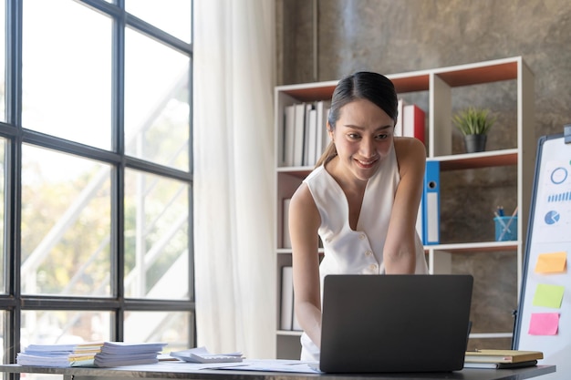 Beautiful young smiling Asian businesswoman working on laptop Asia businesswoman working document finance and calculator in her office