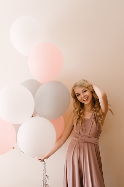 Beautiful young smiling blonde woman with white gray and pink balloons