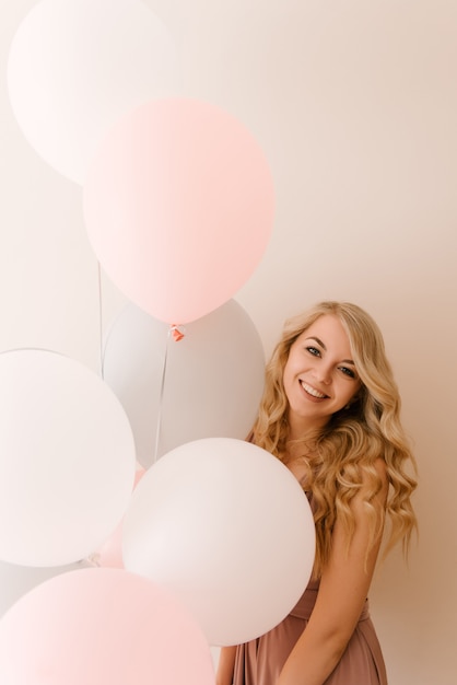 Beautiful young smiling blonde woman with white gray and pink balloons 