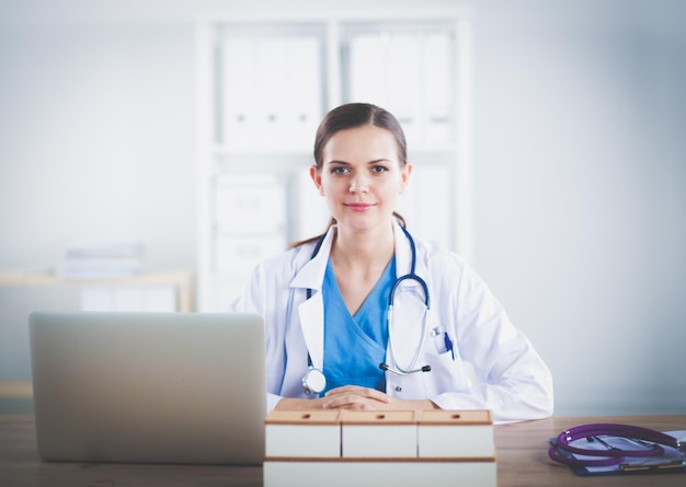 Beautiful young smiling female doctor sitting at the desk and writing female doctor