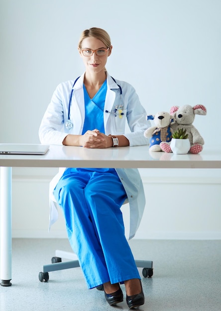 Beautiful young smiling female doctor sitting at the desk