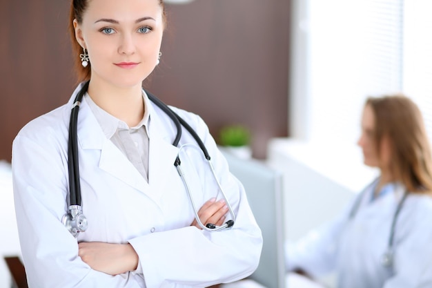 Beautiful young smiling female doctor standing in a hospital with her colleague in the background.