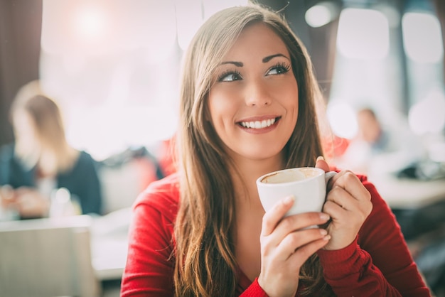 Beautiful young smiling woman relaxing and enjoying a cup of coffee at cafe.