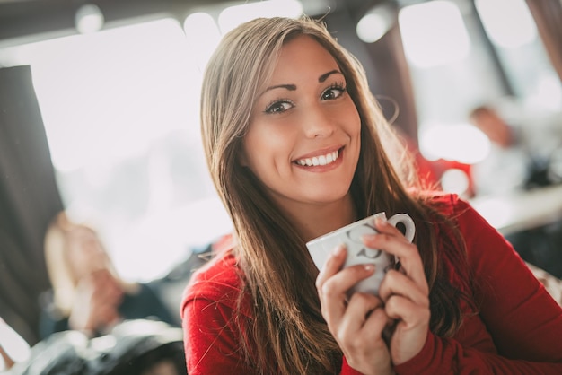 Beautiful young smiling woman relaxing and enjoying a cup of coffee at cafe.