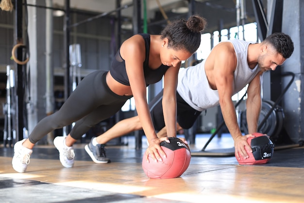 Beautiful young sports couple is working out with medicine ball in gym.