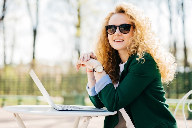 Beautiful young student female with beautiful curly blonde hair elegant dressed using generic laptop computer.