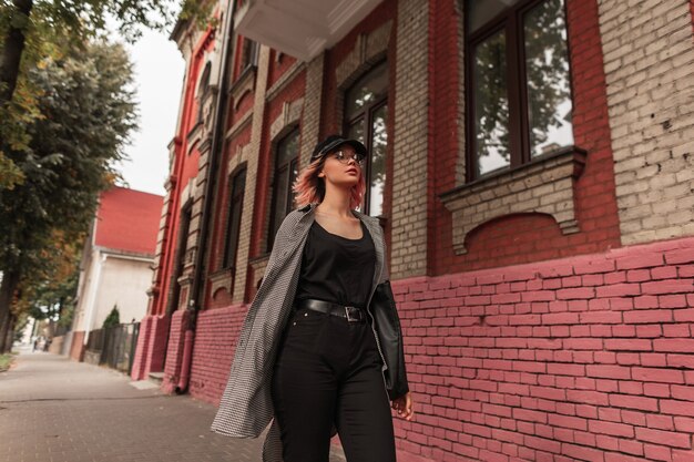 Beautiful young stylish teenage girl in fashionable clothes walks on the street near a vintage building