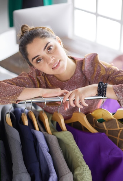 Beautiful young stylist near rack with hangers