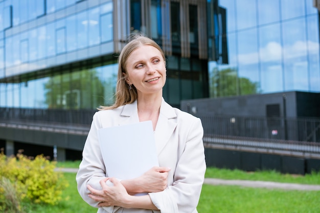 Beautiful young suburban business woman walking in classic urban office buildings holding paper docu...