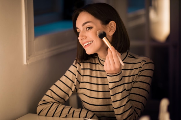 Photo beautiful young woman applying blush with brush