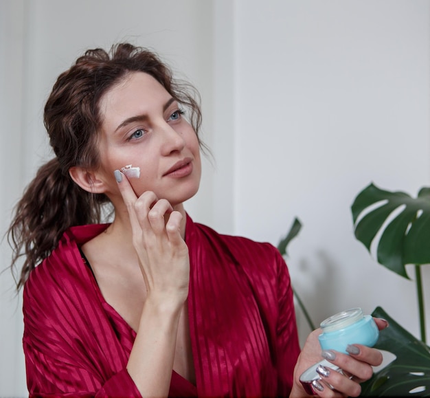 Beautiful young woman applying cream on her face skin rejuvenation