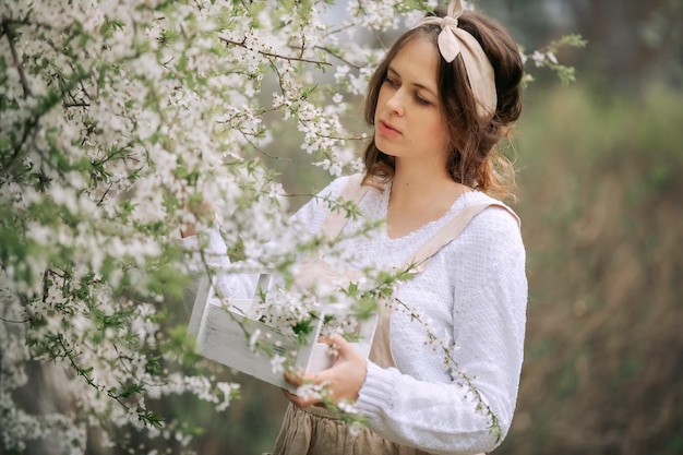 A beautiful young woman in the apron enjoys life in a spring blooming garden with blossom