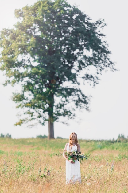 Beautiful young woman on the background of a large tree with a bouquet of flowers in their hands