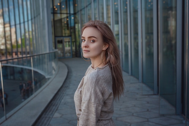 A beautiful young woman in a beige knit dress walks through the streets of Moscow, the famous and popular Zaryadye Park right in the center near the Red Square