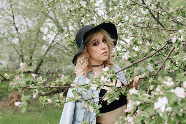 A beautiful young woman in black clothes and a hat in a blooming garden in spring 1