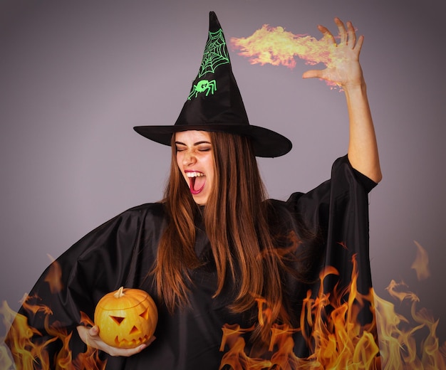 Beautiful young woman in black costume of witch with black hat holding a pumpkin