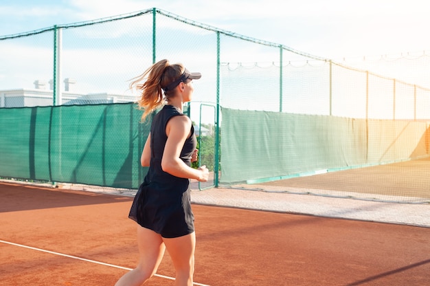 Beautiful young woman in black sports clothes runs around in tennis court