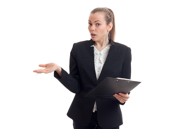 Beautiful young woman in a black suit holding the tablet in her hand and is surprised at camera isolated on white wall