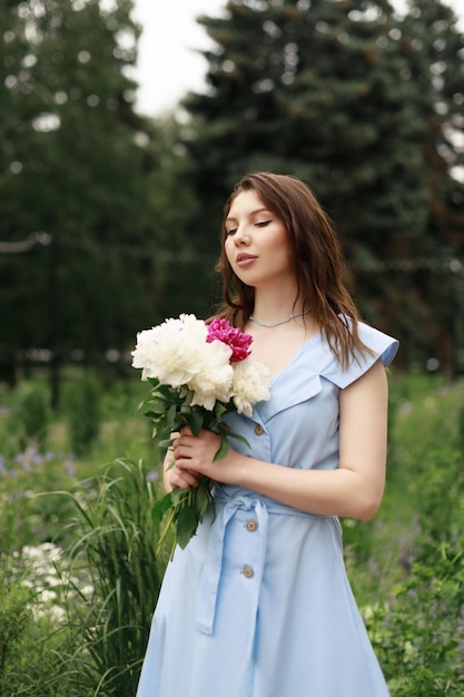 A beautiful young woman in a blue dress with a bouquet of peonies