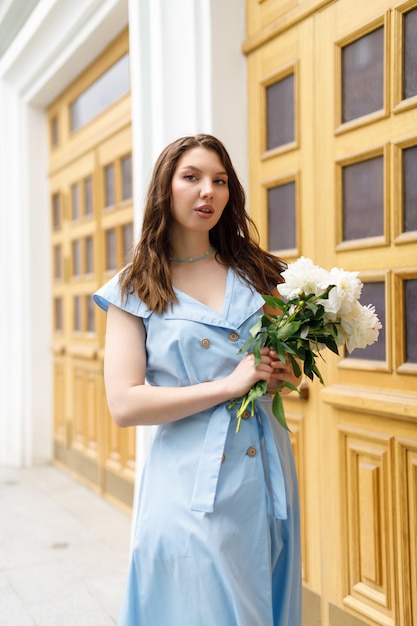 A beautiful young woman in a blue dress with a bouquet of peonies