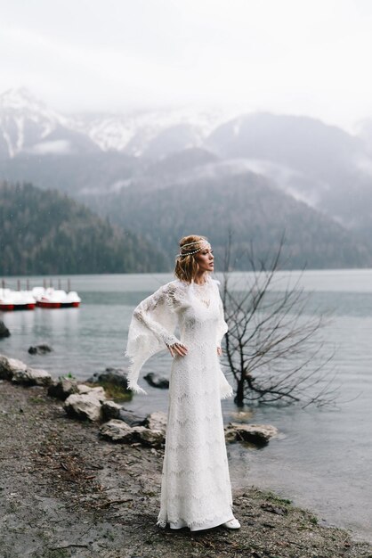 Photo a beautiful young woman bride in a wedding lace dress stands in the middle of a lake and mountains