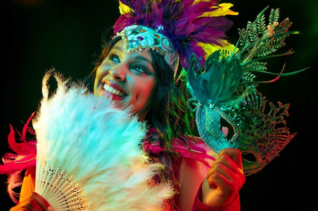 Beautiful young woman in carnival mask and masquerade costume in colorful lights