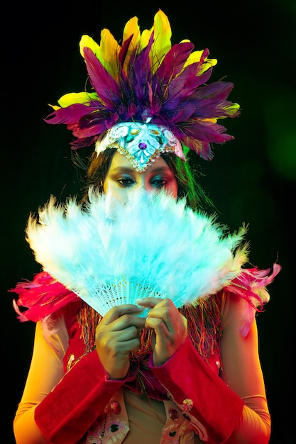 Beautiful young woman in carnival mask and masquerade costume in colorful lights