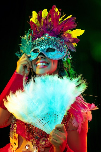 Beautiful young woman in carnival mask and masquerade costume in colorful lights