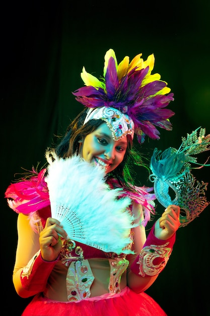 Beautiful young woman in carnival mask and masquerade costume in colorful lights