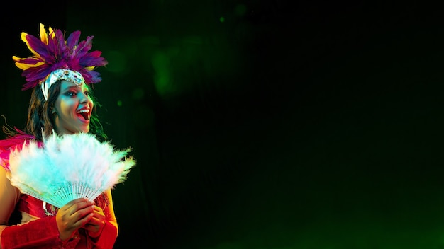 Beautiful young woman in carnival mask, stylish masquerade costume with feathers and sparklers inviting