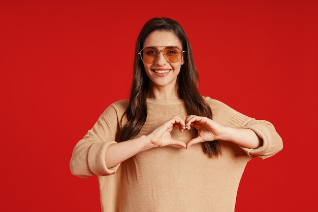 Beautiful young woman in casual clothing smiling and making heart gesture