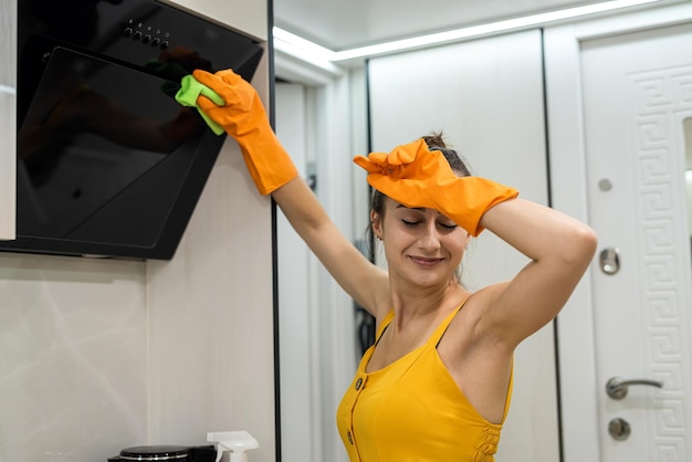 Beautiful and young woman cleaning kitchen hood from dust