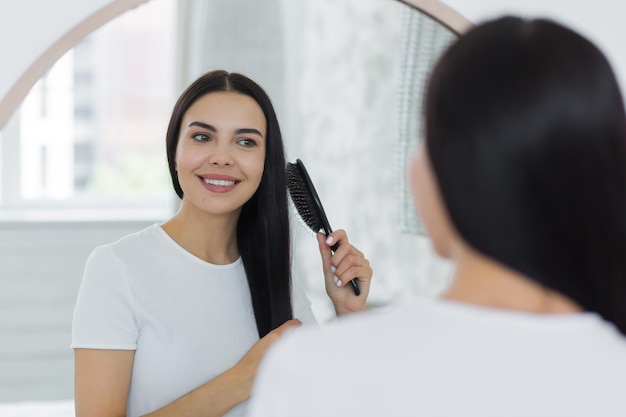 Beautiful young woman combing her hair in the morning looking in a big round mirror and smiling