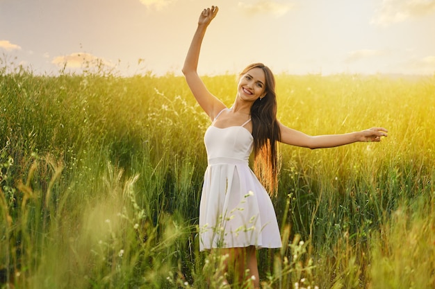 Beautiful young woman dancing in the field over the sunset