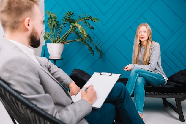 Beautiful young woman discussing her problems with male psychologist sitting on chair