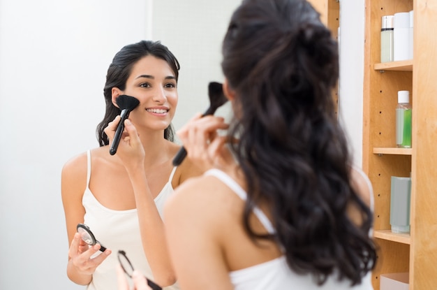 Beautiful young woman doing make up in her bathroom