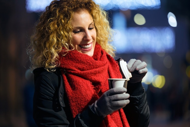 Beautiful young woman drinking coffee in the street at night.