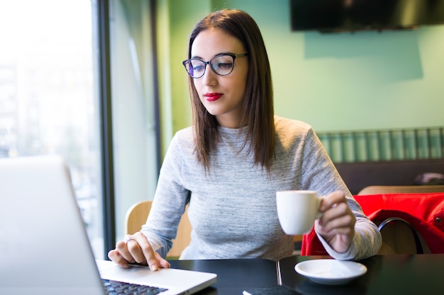 Beautiful young woman drinking coffee while using her laptop in the coffee shop.