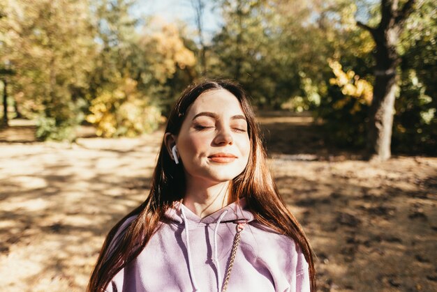 Beautiful young woman in earphones listen music and enjoying autumn weather in the park.