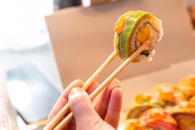 Photo beautiful young woman eating sushi roll at cafe. woman eating sushi set with chopsticks on restaurant.