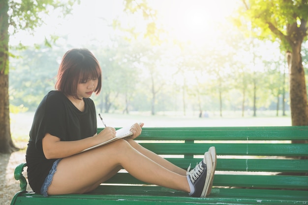 Beautiful young woman enjoying summer on a bench in the garden  writing something on notebook