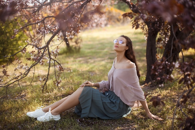 Beautiful young woman enjoying a sunny spring day in a park during cherry blossom season