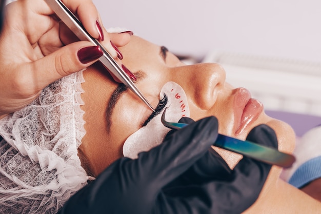 Beautiful young woman at eyelash extension procedure. Cosmetics and body care close up shot.