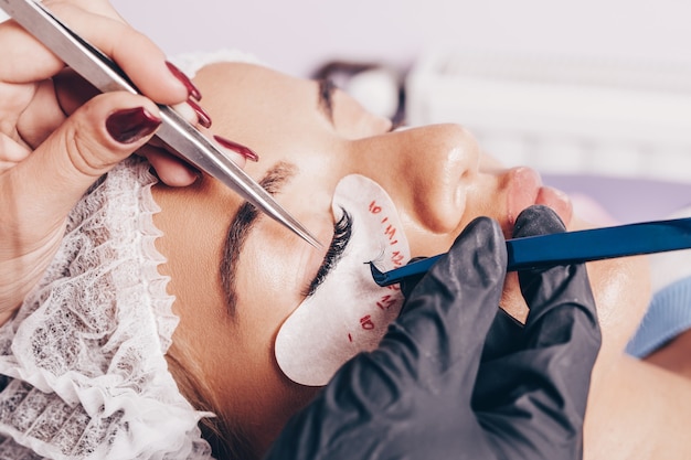 Beautiful young woman at eyelash extension procedure. Cosmetics and body care close up shot.