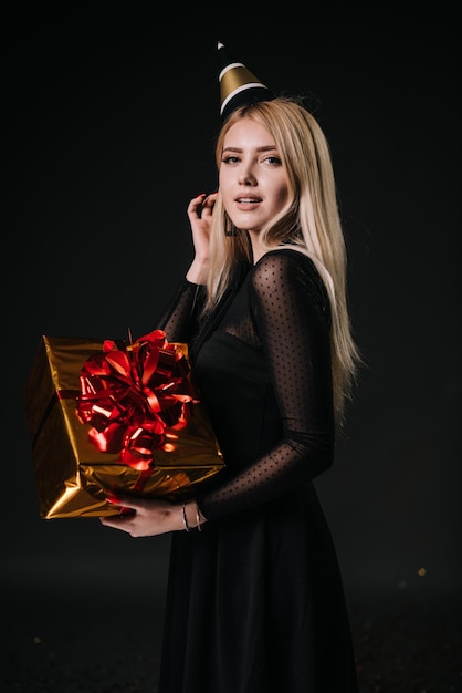 Beautiful young woman in a festive cap holds a holiday box with a gift