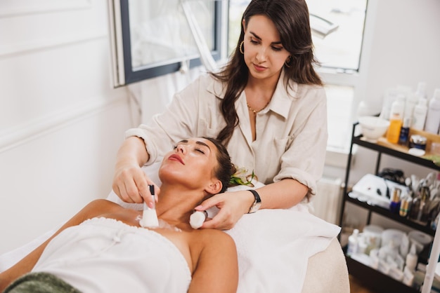 Beautiful young woman getting a cleaning treatment on face and decollete zone at the beauty salon.