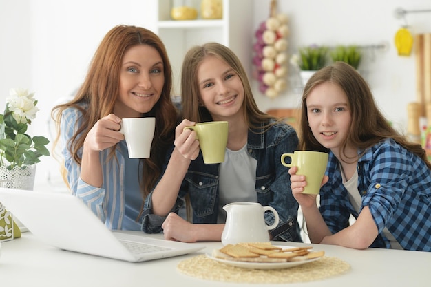 Beautiful young woman and girls sitting at table and using laptop and drinking tea