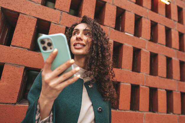 Beautiful young woman in green coat using her cellphone in the city